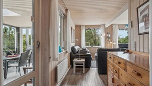 A cozy cabin interior with a wooden ceiling, a sofa, a dining area with chairs, and a view of the outdoors. - 3 bedroom stunning home in Ringkøbing (Ringkøbing)