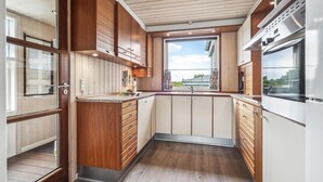 A compact kitchen with wooden cabinets, a built-in oven, and a window providing a view. - 3 bedroom stunning home in Ringkøbing (Ringkøbing)