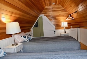 Cozy bedroom with a loft-style design, featuring a bed with a checkered bedspread and bedside tables with lamps.