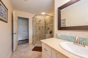 A bathroom with a glass-enclosed shower, a sink with a mirror, and a door leading to another room.