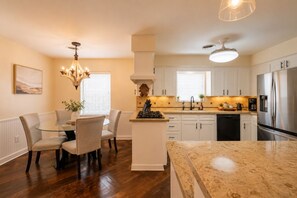 A modern kitchen with white cabinets, a stainless steel refrigerator, and a dining area with a glass table and chairs.