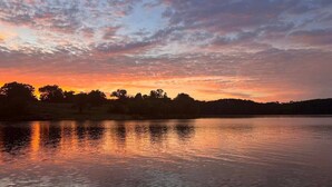 Un lago tranquillo al tramonto con la silhouette di alberi e colline sullo sfondo.