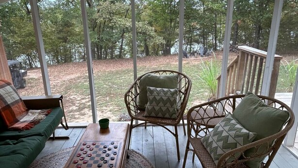 Een overdekte veranda met rieten stoelen, een houten tafel en een groene bank.