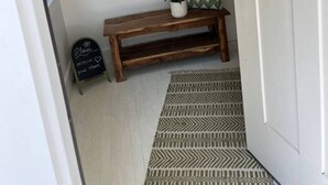 Een hal met een houten bankje, een kleine plant en een schoolbord met een bord.
