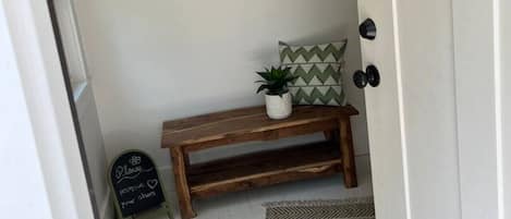 Ein Flur mit einer Holzbank, einer kleinen Pflanze und einem Kreidetafel-Schild.