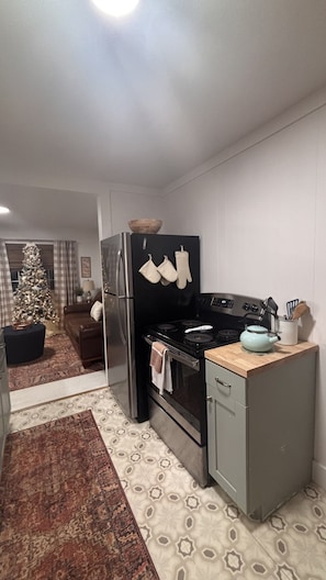 A compact kitchen with a refrigerator, oven, and stove. There is a Christmas tree in the living room.