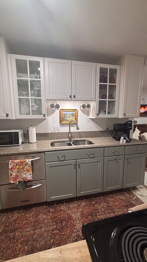 Een keuken met witte kastjes, een dubbele spoelbak, een magnetron en een koffiezetapparaat.