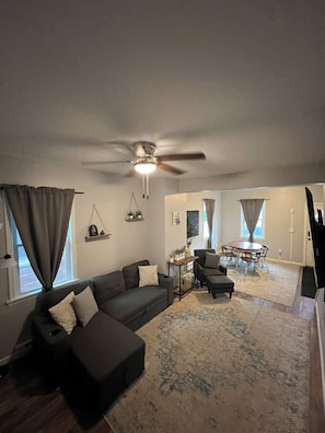 A living room with a sectional sofa, a ceiling fan, a dining table with chairs, and a rug.