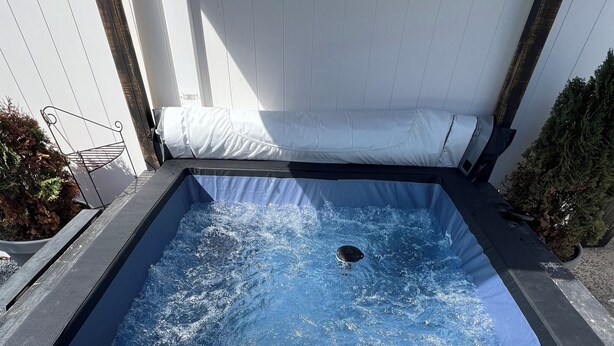 Een rechthoekig bubbelbad met een zwart frame, omgeven door een witte hek en een kleine plant in een pot aan de linkerkant.