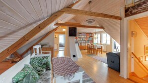 Une chambre mansardée chaleureuse, avec un plafond en pente, un escalier en bois, un lit recouvert d’une literie à motifs floraux, une petite table et une bibliothèque remplie de livres.