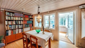 Une salle de lecture accueillante, avec des étagères en bois, une table entourée de chaises et une grande fenêtre donnant sur l’extérieur.