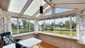 Une véranda avec des murs en bois et de grandes fenêtres, une table et une chaise.