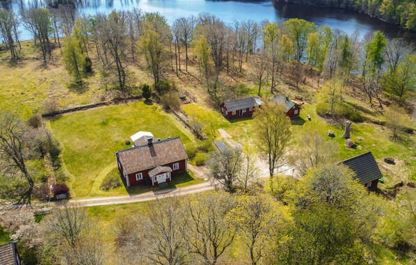 Vue aérienne d’une propriété rurale comprenant une maison principale, un petit bâtiment rouge et un étang.