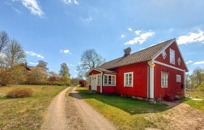 Une maison en bois rouge, avec un toit recouvert de tuiles, une cheminée bien visible et un chemin de gravier menant à l’entrée.