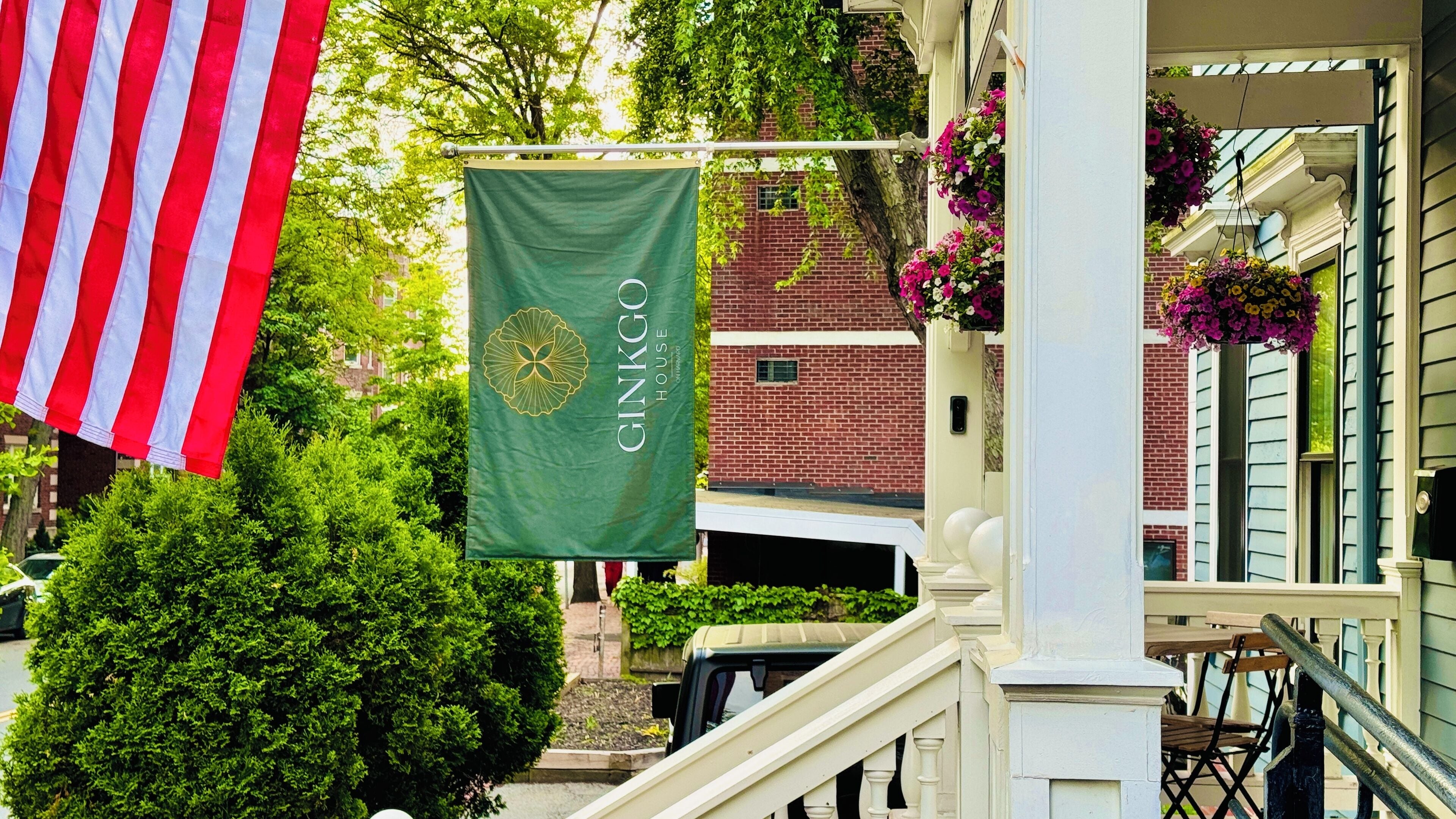 A green banner with "GINKGO HOUSE" hanging on a building, a white and red striped flag, and a brick building with a white porch.