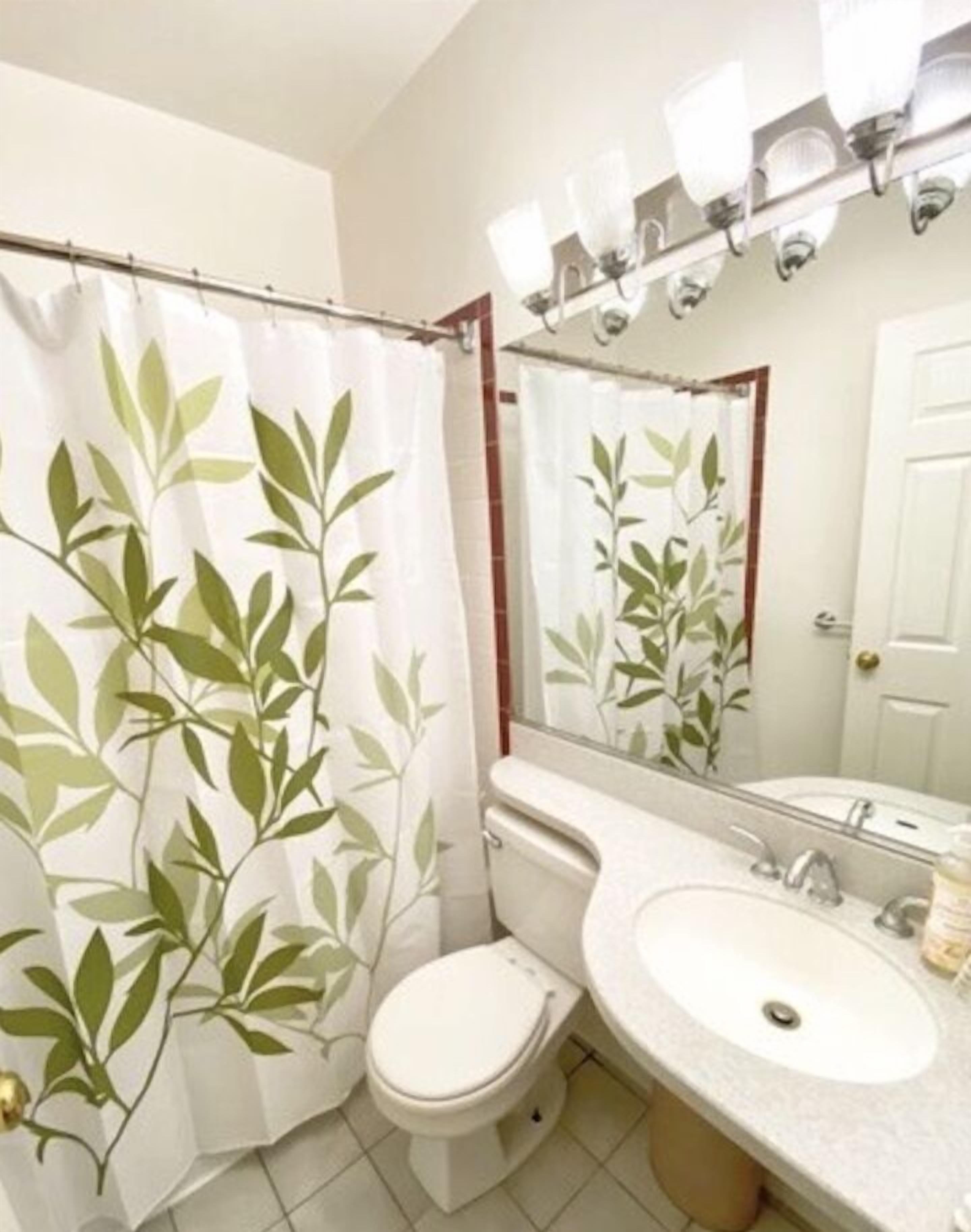 Un baño con inodoro, lavamanos y cortina de ducha estampada con hojas.