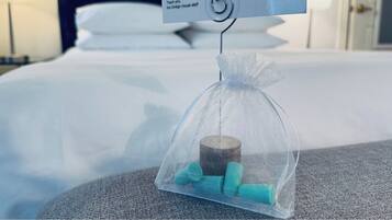 A clear plastic bag containing a rolled-up towel and two bath sponges hanging from a hook on a bed.