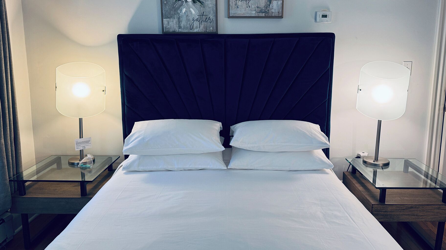 A hotel room with a large bed, two bedside tables, two wall-mounted lamps, and a thermostat on the wall.