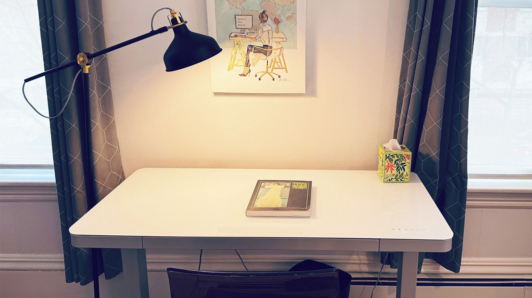 A white desk with a black desk lamp, a framed artwork, a book, and a tissue box.