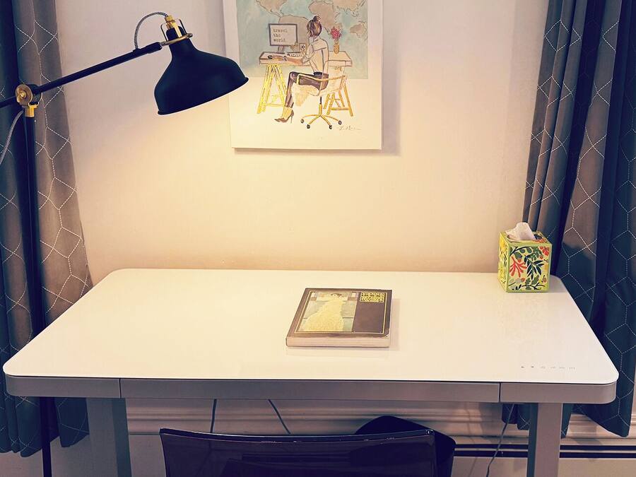 A white desk with a black desk lamp, a framed artwork, a book, and a tissue box.