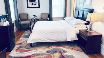 A hotel room with a bed, two chairs, a small table with a bonsai tree, a nightstand with a lamp, and a water dispenser.