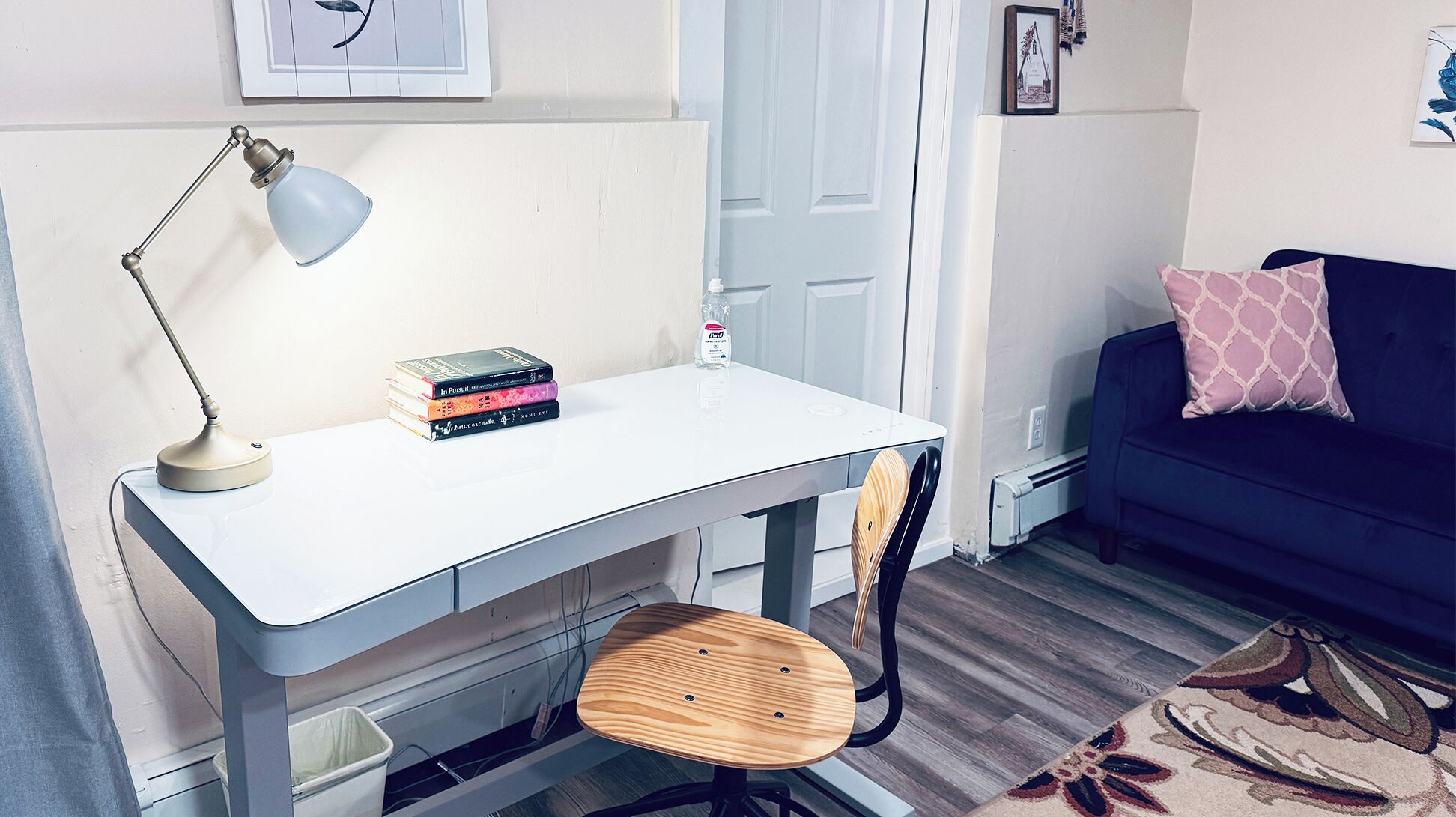 Una habitación compacta con escritorio blanco, una silla, sofá azul y alfombra estampada.