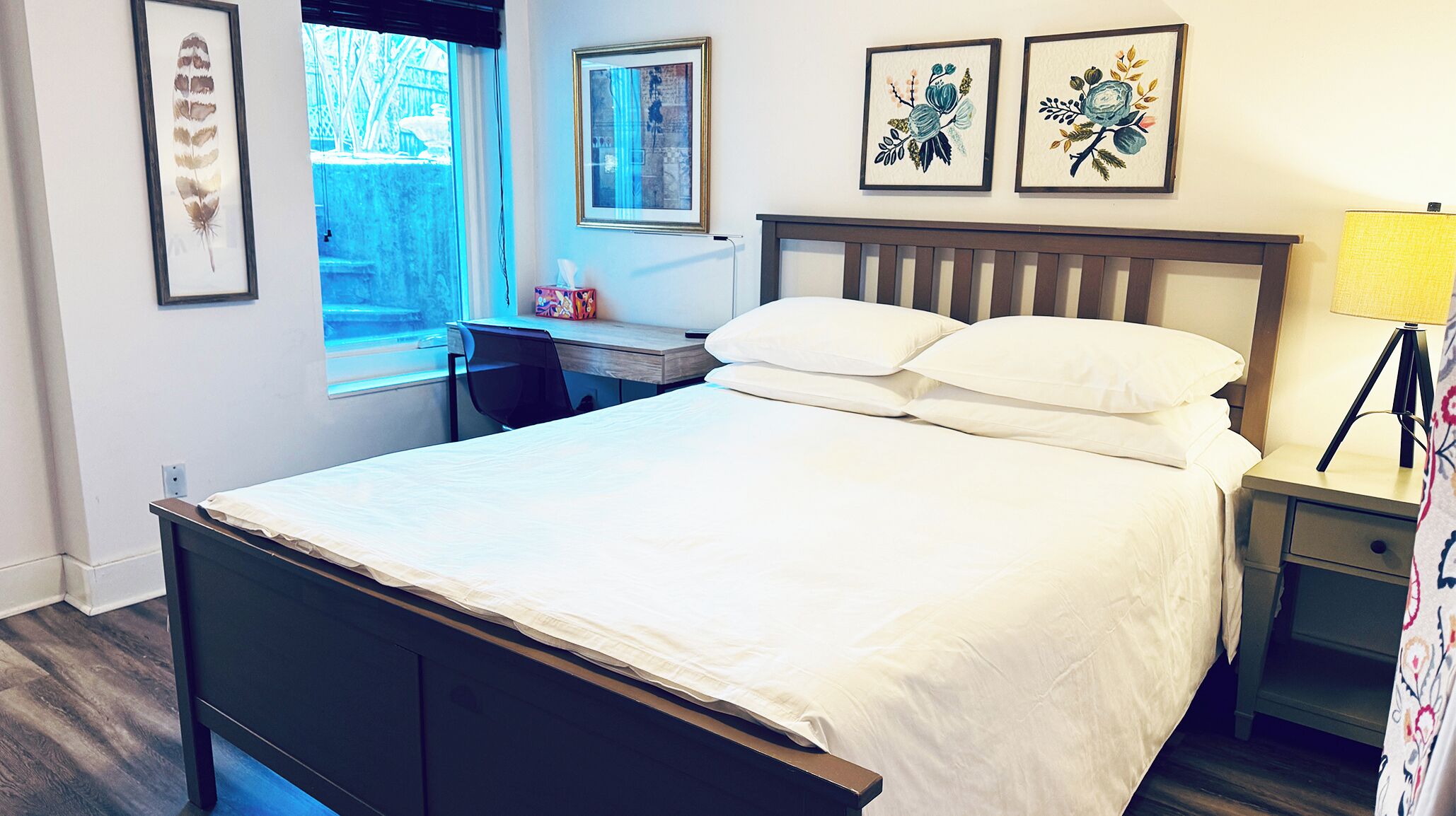 A bedroom with a bed, a desk, and a chair. There are framed pictures on the wall.