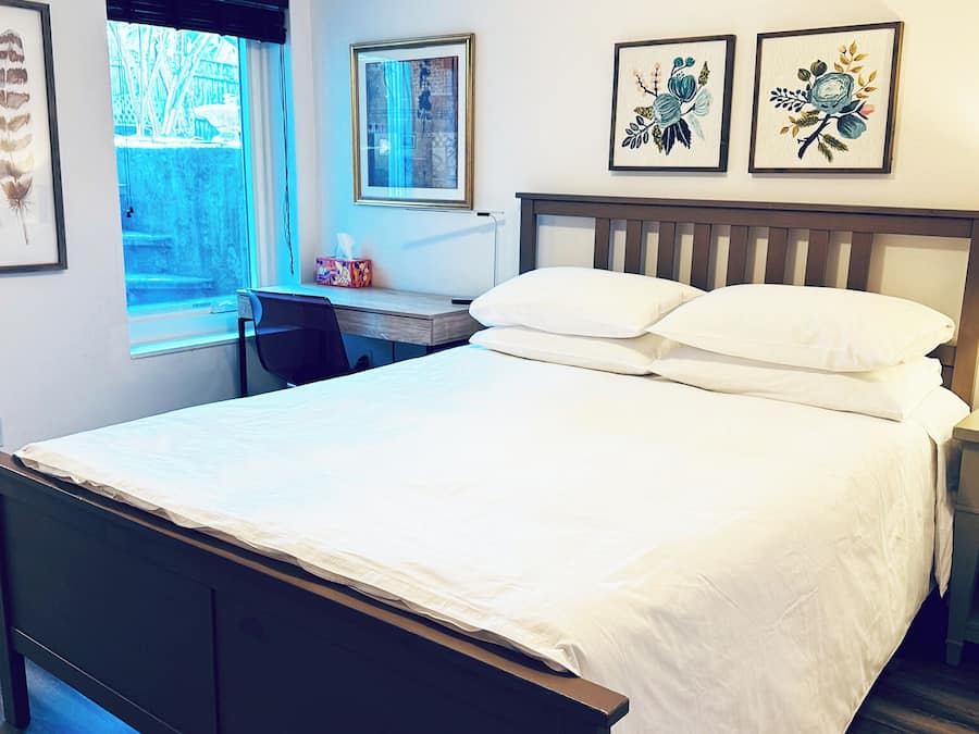 A bedroom with a bed, a desk, and a chair. There are framed pictures on the wall.