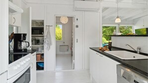 A modern kitchen with white cabinetry, a coffee machine, a sink, and a view of greenery outside.