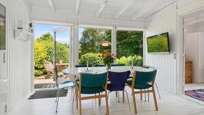 A conservatory with a round table, four chairs, a vase with flowers, and a TV mounted on the wall.