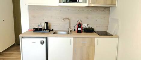 Una kitchenette compacta con microondas, cafetera, hervidor y un refrigerador pequeño.