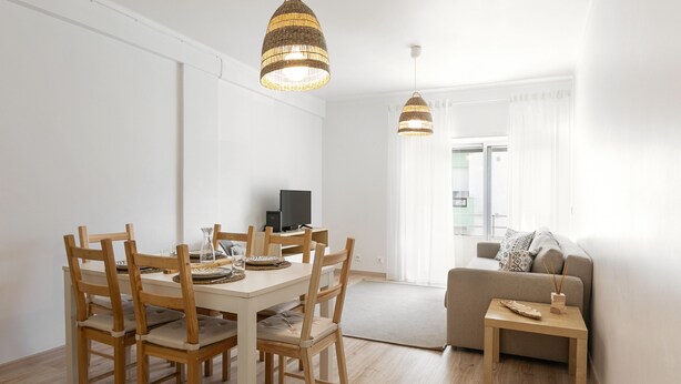 Una sala de estar moderna con comedor, que presenta una mesa y sillas de madera, un sofá y dos lámparas colgantes.