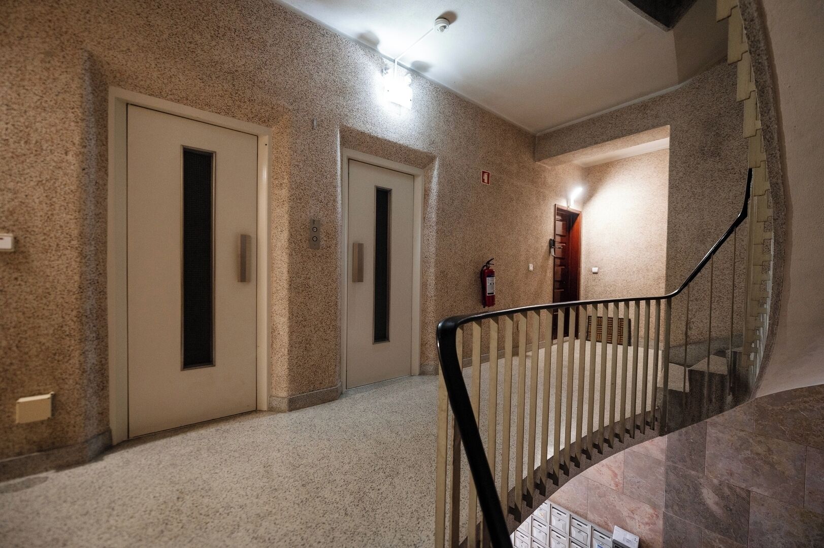 A hallway with two doors, a fire extinguisher, and a staircase.