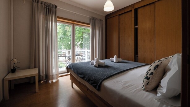 Ein Schlafzimmer mit einem großen Bett, Holzvertäfelung, einem Nachttisch mit Pflanze und Blick ins Freie.