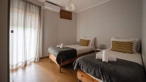 Ein Schlafzimmer mit zwei Betten, Holzboden, einer weißen Klimaanlage und einem Fenster mit Vorhängen.