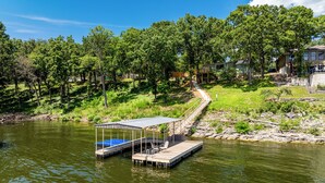 A dock with a covered seating area, a pathway leading to a house, and a forested hillside.