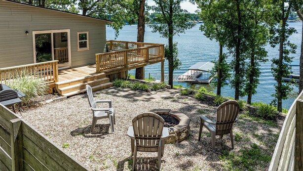 A cabin with a deck overlooking a lake, outdoor seating, and a fire pit.