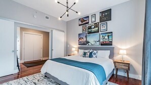 Un dormitorio moderno con una cama grande, piso de madera, una puerta blanca y un muro decorado con cuadros.