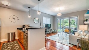 Una cocina moderna con una isla central, un comedor con mesa y sillas, y una sala de estar con sofá y lámpara.