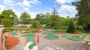 A miniature golf course with a wooden bench, surrounded by trees and a clear sky. - Deluxe Cabin6 Within Campground (Mifflinburg)