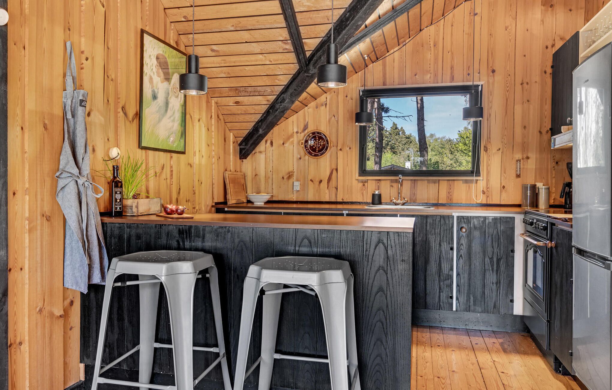 Un interior de madera con zona de cocina, que incluye un refrigerador, estufa y taburetes de bar.
