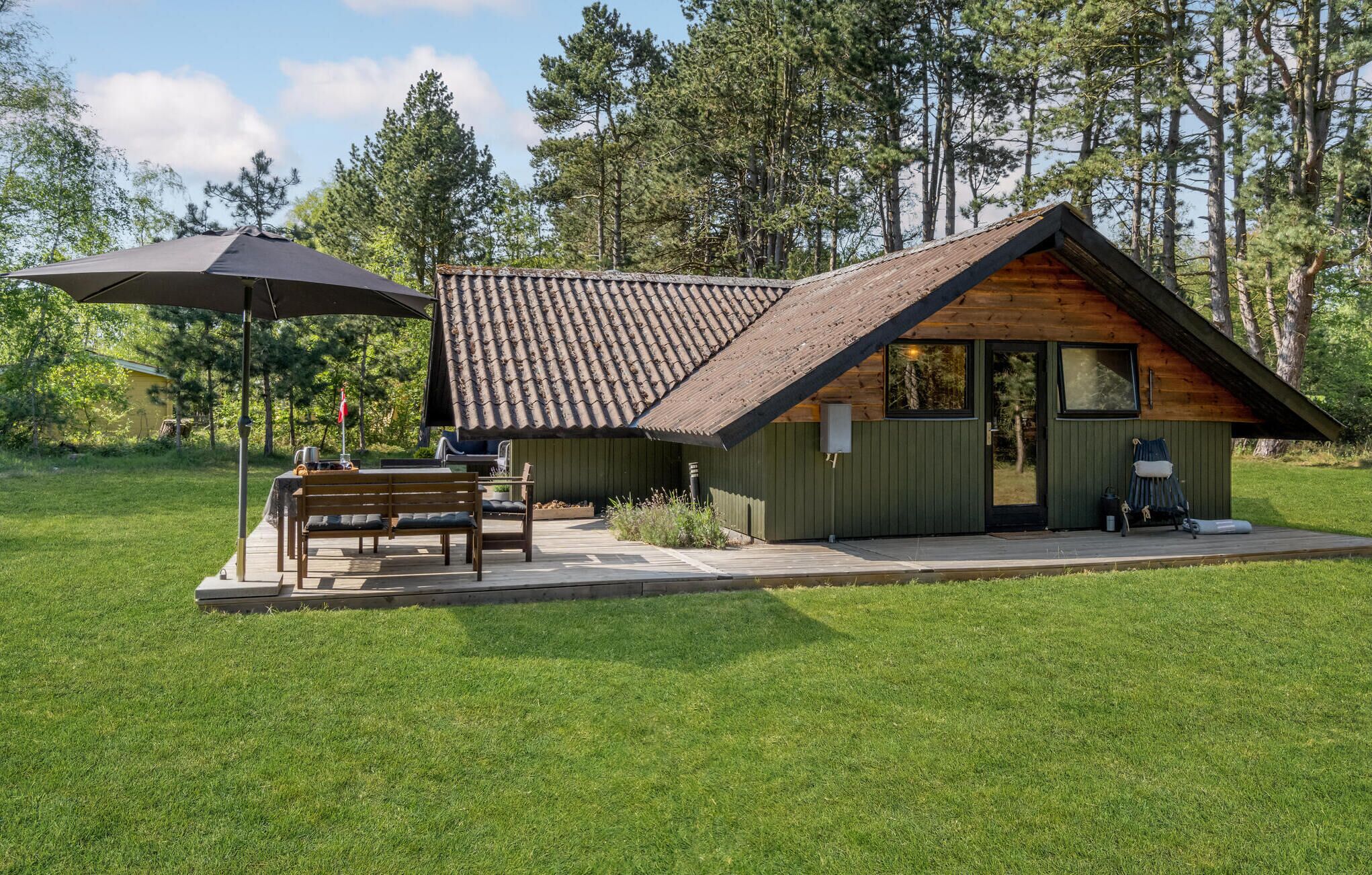 A rustic cabin with a tiled roof, a wooden deck, and a bench.