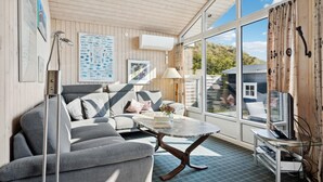 Una sala de estar acogedora con un sofá, una mesa de centro y un televisor. Hay cuadros enmarcados en la pared y una ventana con cortinas.