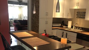 A modern kitchen with a central island, bar stools, and pendant lighting. - Oyster Cottage  - walk to shops , Mainstay music venue and the Bay! (Rock Hall)