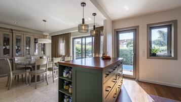 A modern kitchen with a central island, dining area with chairs, and large windows offering views of greenery.