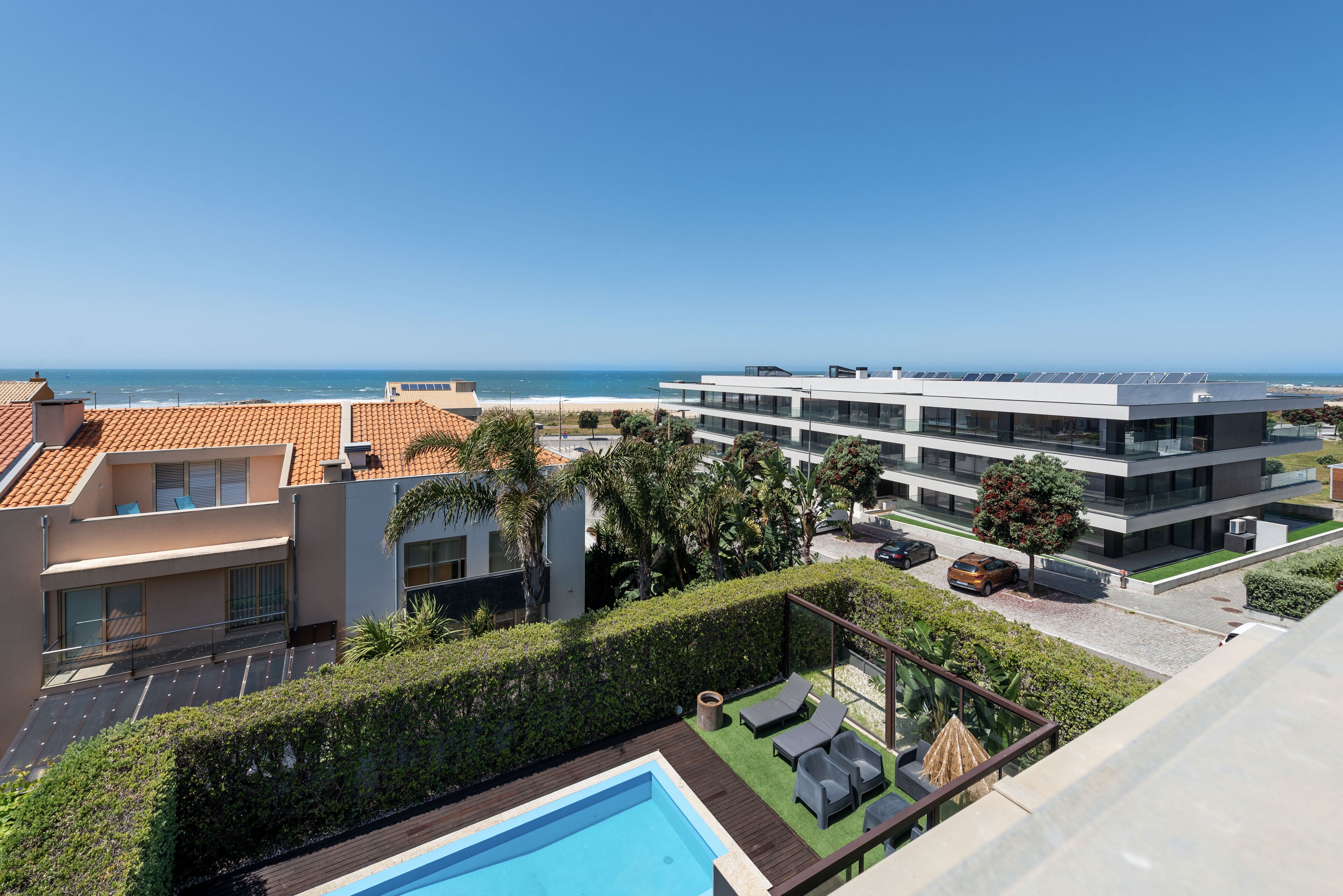 A modern building with a rooftop pool, a clear view of the ocean, and a well-maintained garden area.
