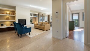 A modern living room with a beige sofa, blue armchairs, and a flat-screen TV. There are built-in shelves and a fireplace. - Atlantic House - Beachfront Luxury House (Vila Nova de Gaia)