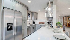 A modern kitchen with stainless steel appliances, a large island with seating, and pendant lighting. - Beautiful 3 bedroom 2 bathroom waterfront home on Drs. Lake (Orange Park)