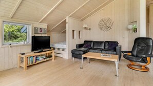 A cozy living room with a wooden ceiling, a black leather sofa, a wooden coffee table, a black leather chair, and a television on a wooden stand.