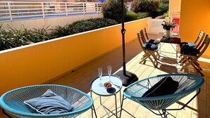 Ein Balkon mit Gartenmöbeln, darunter zwei blaue Stühle und ein Tisch mit einer Glasbowl und zwei Gläsern.